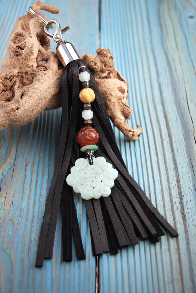 chinese jade floral pendant on beaded strand with carnelian jade and aventurine on a black leather tassel key fob purse charm on top of blue wood table