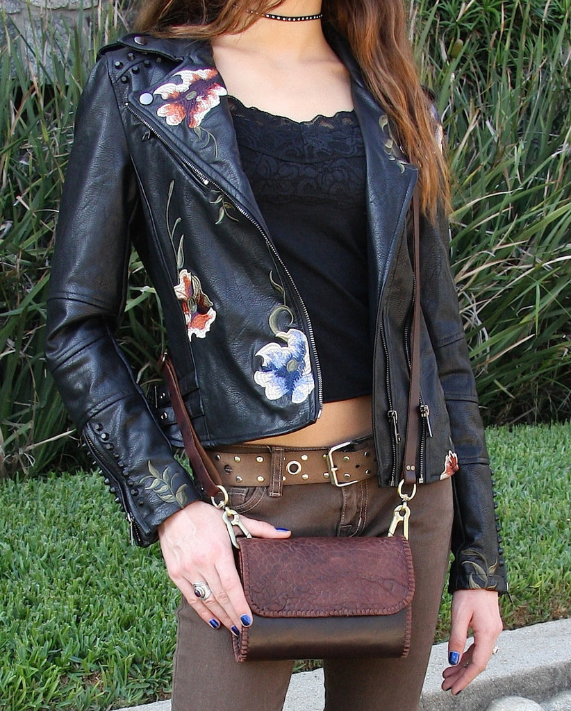 Crocodile embossed lambskin crossbody bag on woman wearing black embroidered leather jacket and brown jeans