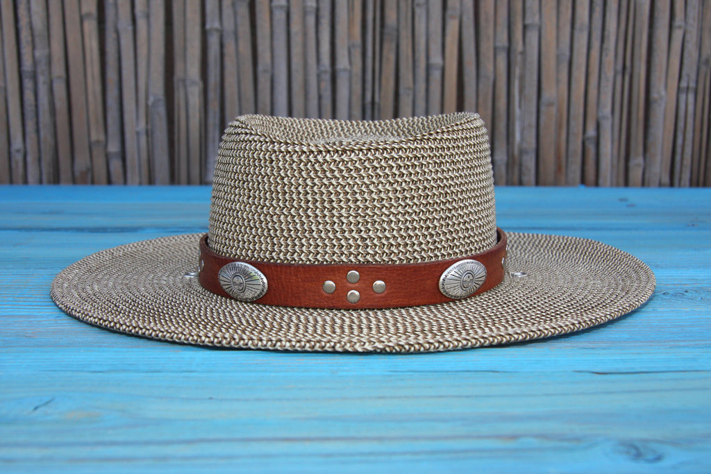 distressed brown leather southwestern style hat band with silver tone studs and eagle conchos on straw hat sitting on blue wood table 
