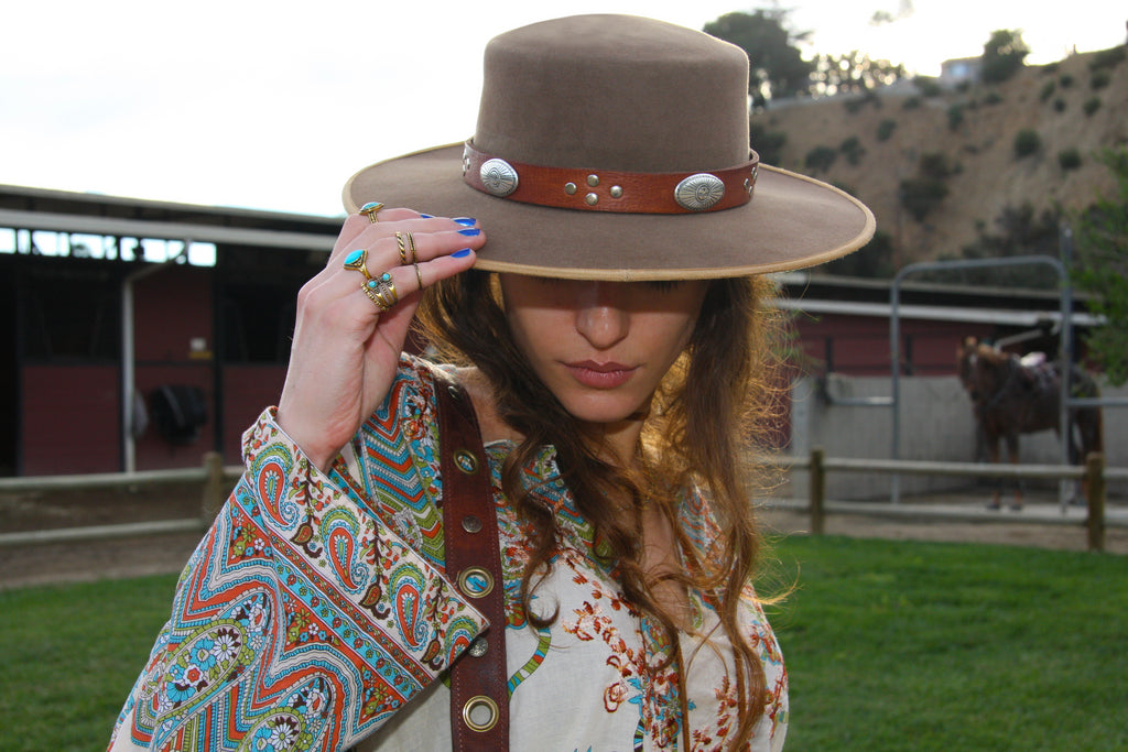 Girl at horse stables wearing tan bolero hat with handmade brown leather hat band adorned with southwestern eagle conchos
