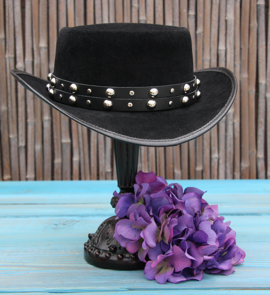 bohemian black leather top hat with  black leather studded hat band on blue wood table with bamboo background