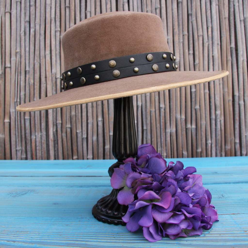 tan beaver felt bolero hat with black antique brass studded leather hat band on blue wooden table with bamboo background