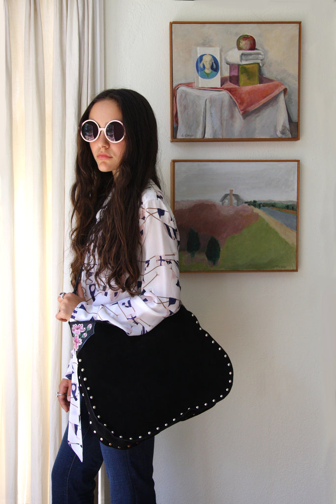 girl standing in front of paintings with black suede studded tote with hand tooled cherry blossom accents