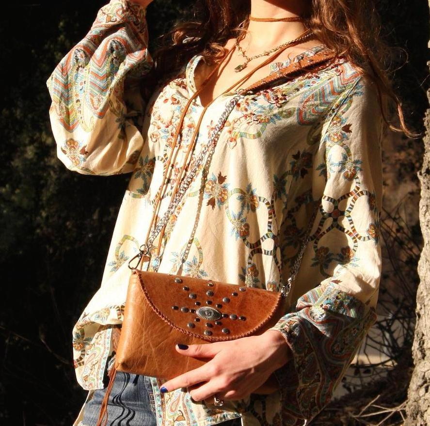 woman wearing tan envelope bag with eagle concho studded detail on front flap and chain shoulder strap  