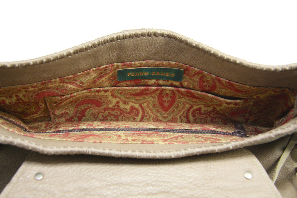 Beige saddle bag purse with metallic fringe inside of bag lined with orange and red paisley print fabric