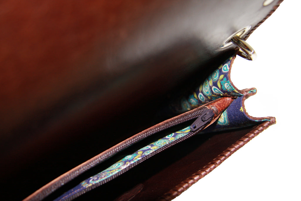 brown studded crossbody bag inside lined with vibrant blue and turquoise printed fabric and middle zipper pocket close up