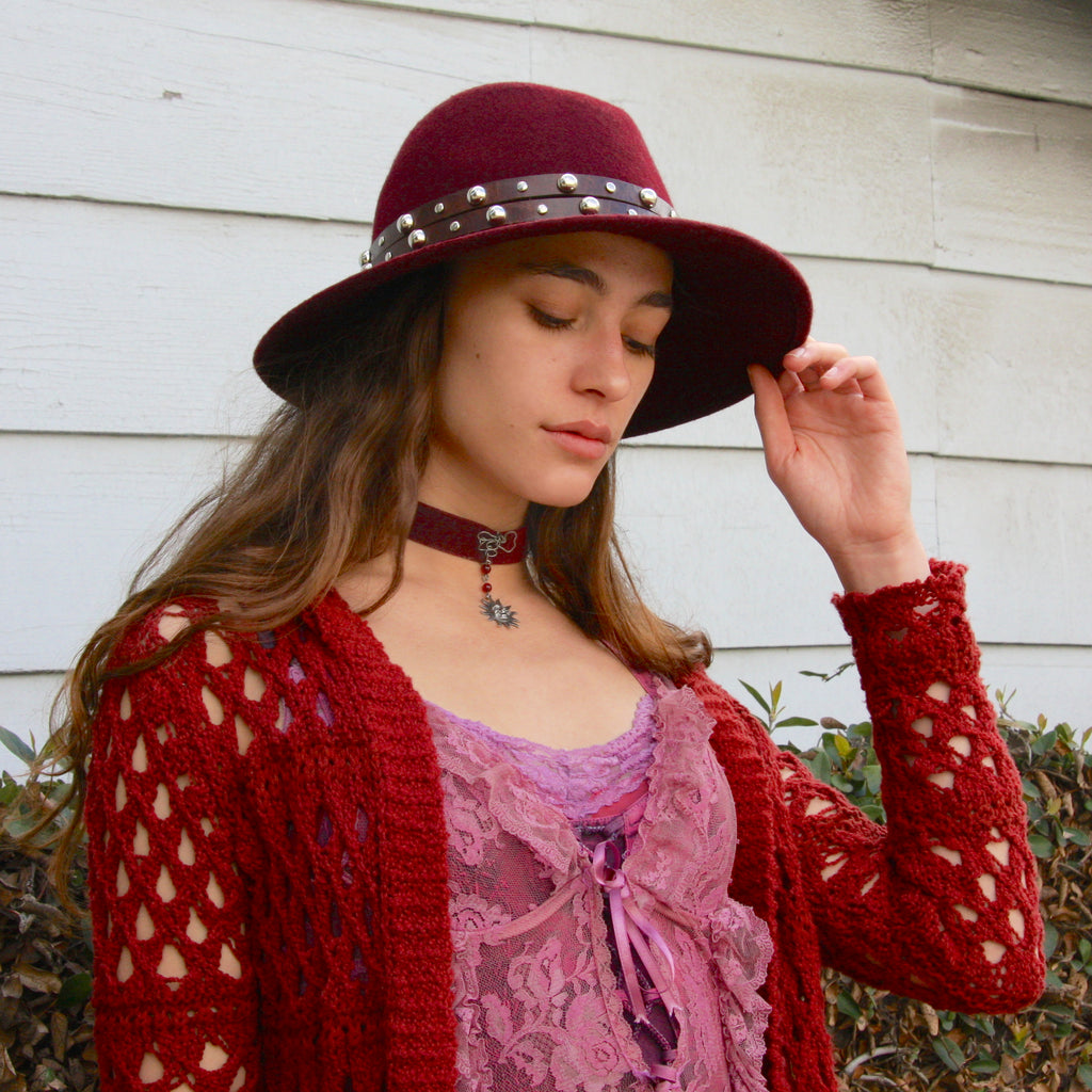brown double strap studded leather hatband on red fedora hat worn by beautiful woman in pink lace dress